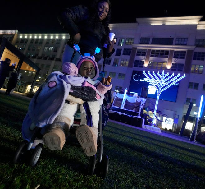 One-year-old Zamara Vasquez finishes her doughnut while with her mother, Portia Reed, of Milwaukee while at the Chanukah Festival and Gelt Drop, to kick off the first day of Chanukah, in The Yard at Bayshore in Glendale on Thursday, Dec. 7, 2023. The largest Hanukkah festival in Wisconsin, hosted by Lubavitch of Wisconsin, included live music, a giant Menorah lighting, and a mega gelt and gift drop.